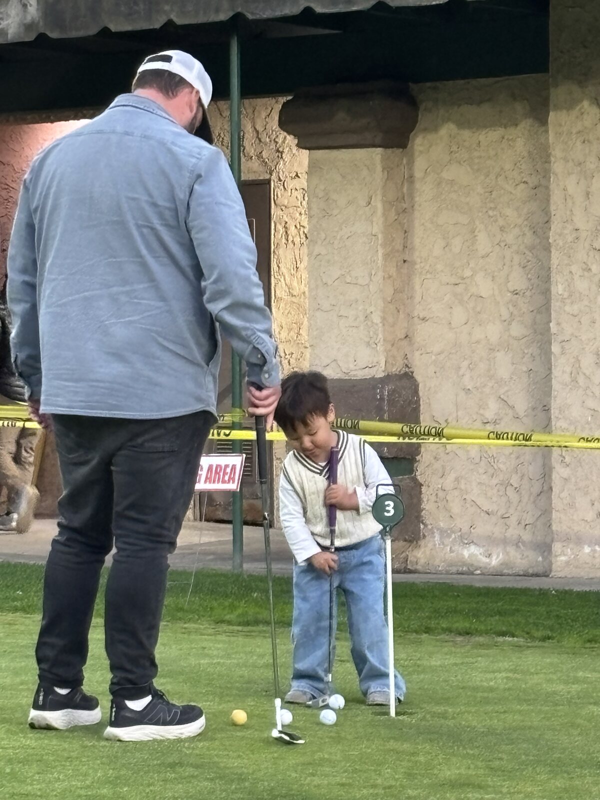 A father and son practicing on the putting green near hole 3