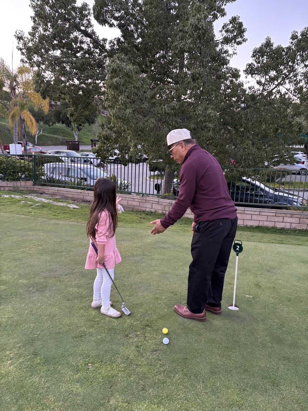 An instructor guides a young golfer's putting stroke on the 18-hole course