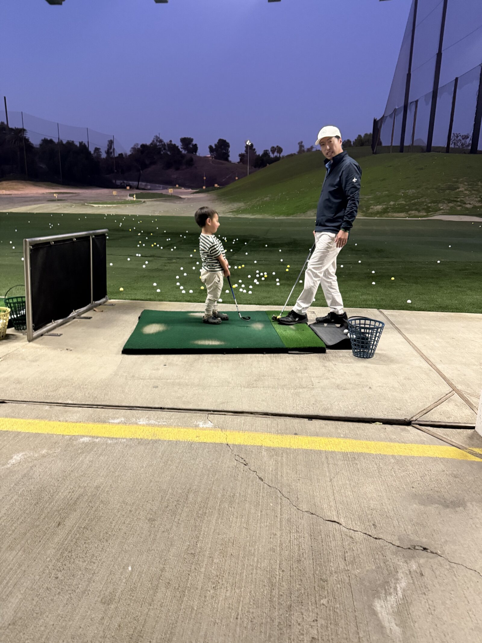 A father and son at the driving range under the lights at dusk