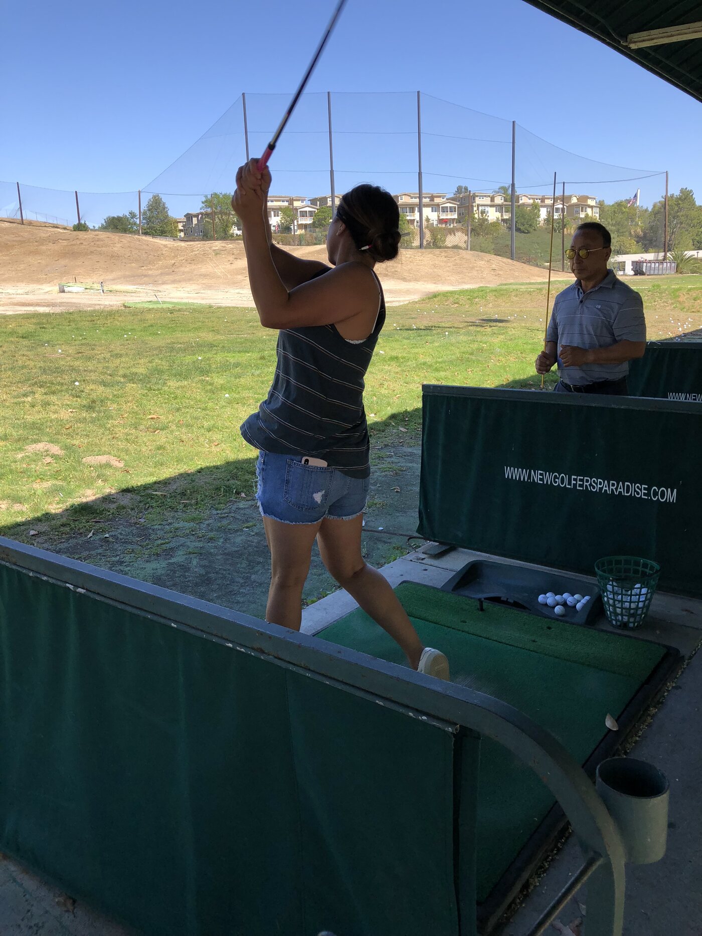 A golfer mid-swing at a covered driving range stall at Golfer's Paradise, real on-site signage visible