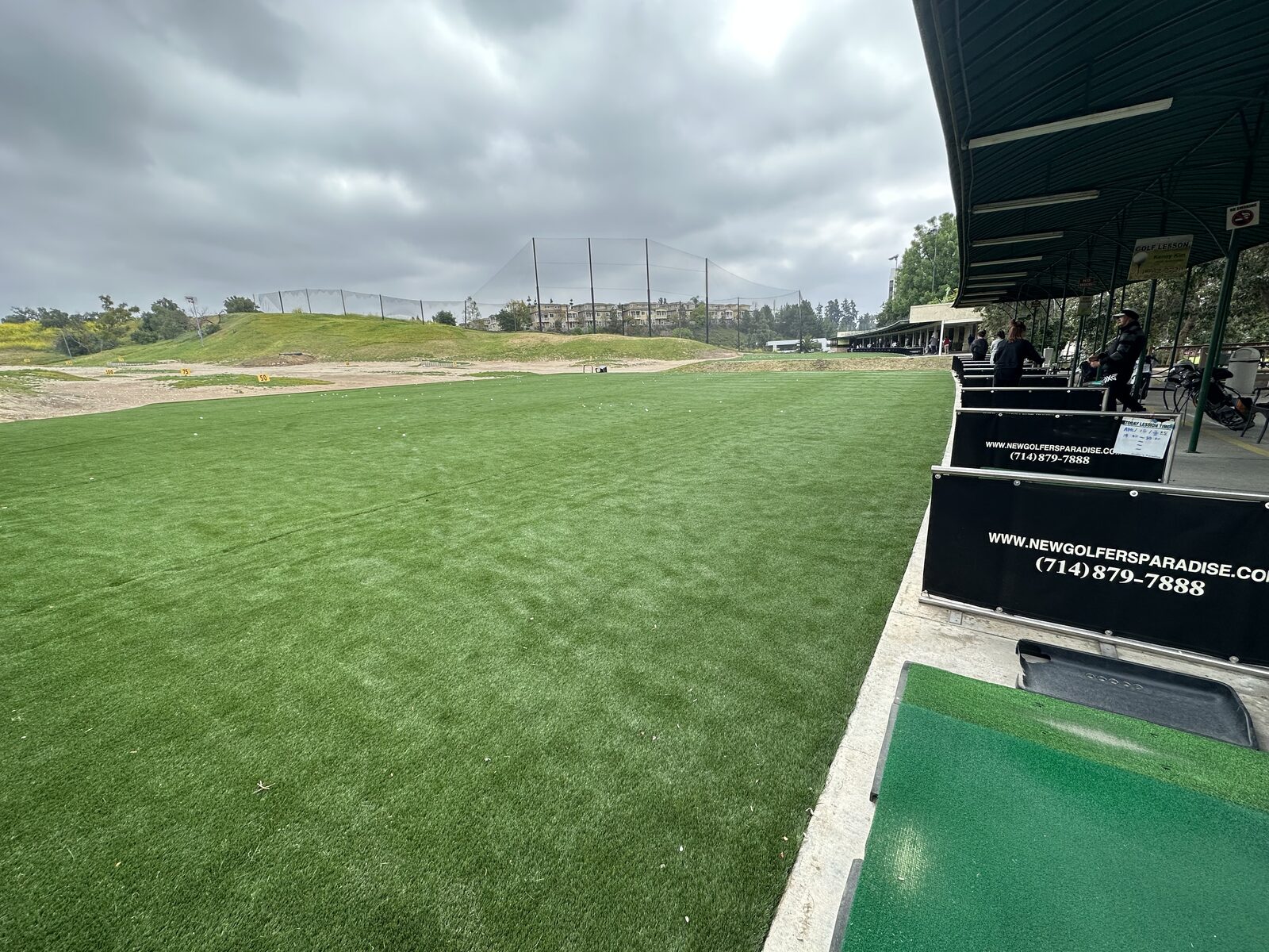 A wide view down the real-grass driving range toward the yardage markers and practice bunkers at Golfer's Paradise